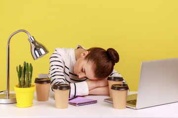 Exhausted fatigued woman office manager sleeping at workplace, lying surrounded by coffee cups,...