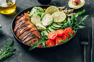 Healthy buddha bowl lunch with grilled chicken arugula, avocado, brussels sprouts, tomato, cucumber and chickpea