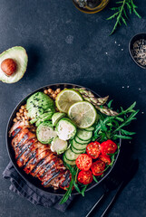 Healthy buddha bowl lunch with grilled chicken arugula, avocado, brussels sprouts, tomato, cucumber and chickpea