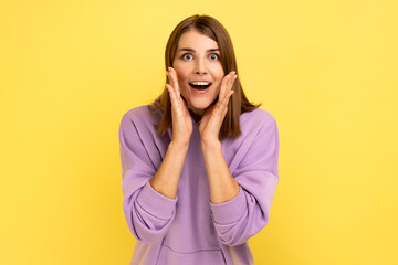 Wow, unbelievable. Excited amazed woman touching face and shouting in surprise, shocked by unexpected win, crazy news, wearing purple hoodie. Indoor studio shot isolated on yellow background.