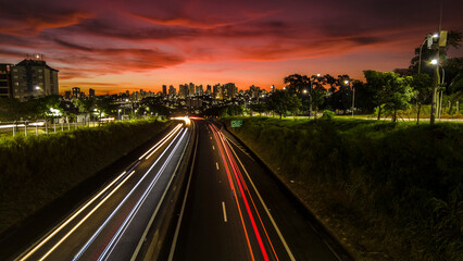 Fototapeta na wymiar Trail of light caused by vehicular traffic in SP-294, Comandante Joao Ribeiro Barros Highway with buildings from downtown in the background, in Marília,