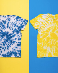 Yellow and blue T-shirts painted in tie dye style on a yellow and blue background. Flat lay.