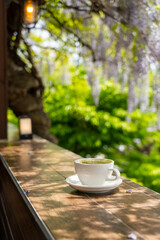Hot cafe latte in a white ceramic cup tea set with purple wisteria flowers hanging at the garden in South Korea