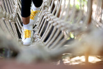 Little child girl play walking on rope bridge on adventure park, close up
