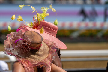 A couple of attendees at a horse race, wearing fancy hats.