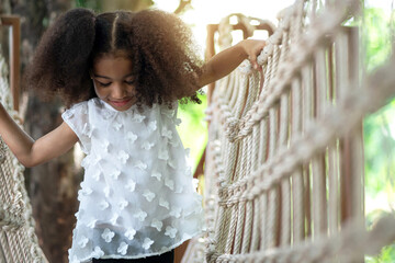 Happy little girl climbing on the bridge in adventure park, having fun at playground on a sunny day