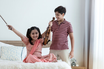 Indian brother and sister, girl practicing her violin in bedroom, older brother suggested playing the violin to his sister, family relationship concept