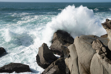 large ocean waves crashing over rock boulders