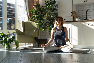 Middle aged woman practicing meditation at home, calm senior middle aged lady in lotus pose doing...