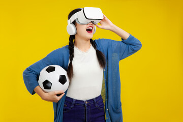metaverse sport concept, amazed asian girl football fan in VR headset holding soccer ball and...