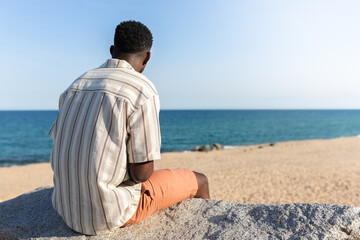 Back view of black man relaxing looking at the ocean. Copy space. - Powered by Adobe