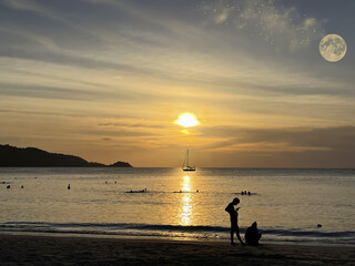 Sunset over the sea. People on the beach. Swimming people. Beautiful sky with clouds, sun, stars, moon. Reflection on the water surface. Golden glow, sunshine. Sand coast. Tropical paradise. Island.  