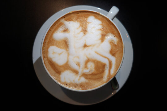 A cup of coffee with Unicorn shape latte art on a black background. Top view image.