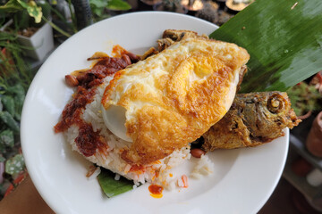 Nasi lemak set with ikan goreng, a traditional Malay curry sambal paste rice dish served with fried fish, egg,  and anchovy. Selective focus image.