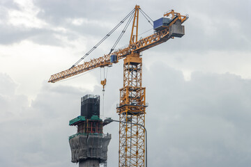 Construction of a concrete pillar using a high-rise crane, on a background of rainy clouds