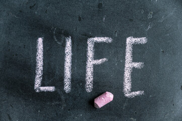 Life. A word written in pink chalk on a black chalkboard. Handwritten text. A piece of colored chalk hangs next to it.