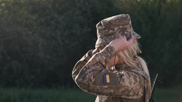 Female Soldier Puts On Camouflage Hat On Head Outdoors Close Up And Looking At The Camera, Profile View