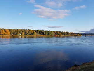Sunny blue river landscape with trees in autumn colors.