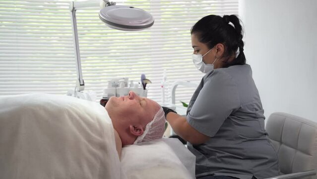 Cosmetologist applying cosmetic mask on man's face in spa salon