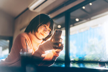 Young adult happy asian using mobile phone for social dating online application at indoor cafe with warm light