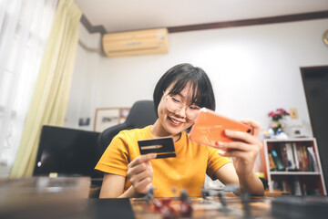 Young adult asian woman using smartphone and credit card shopping for hobby lifestyle at home