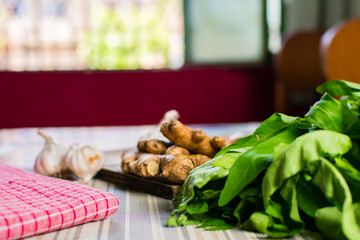 Whole raw fresh ginger place on a wooden chopping board surrounded by kitchen towel, whole garlic and herbs