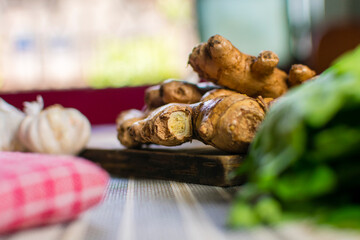 Whole raw fresh ginger place on a wooden chopping board surrounded by kitchen towel, whole garlic and herbs