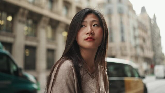 Beautiful Asian long haired woman standing on the street with passing cars on background. Asian girl walking in downtown alone