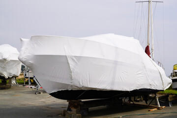 boat out of water protected by a plastic film for wintering ship under tarpaulin tarp - obrazy, fototapety, plakaty