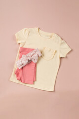  Yellow children's t-shirt and folded pink pants on a pink background. Fashionable image for a girl.