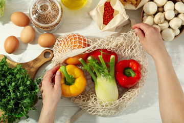 Female hands get food from string bag on white wooden table
