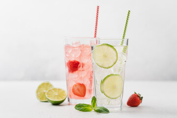 Lime mojito and strawberry lemonade with ice in tall glasses on light gray background. Berry...