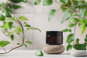 Cosmetic glass jar on stone podium with green plants on light background. Skincare products, natural cosmetic. Beauty concept for face and body care