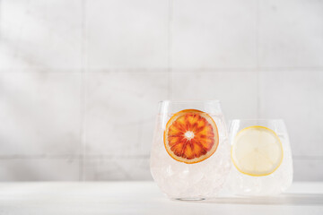 Cold water with red orange and lemon in glasses on white background. Refreshing lemonade, summer drink, cocktail, soda. Empty copy space