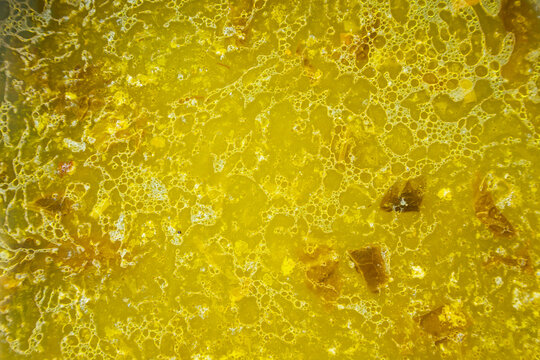 The texture of the surface of a yellow vegetable soup with droplets of fat on the surface.