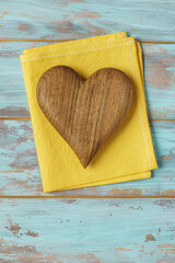 Wooden heart on yellow cotton napkin on shabby cyan table