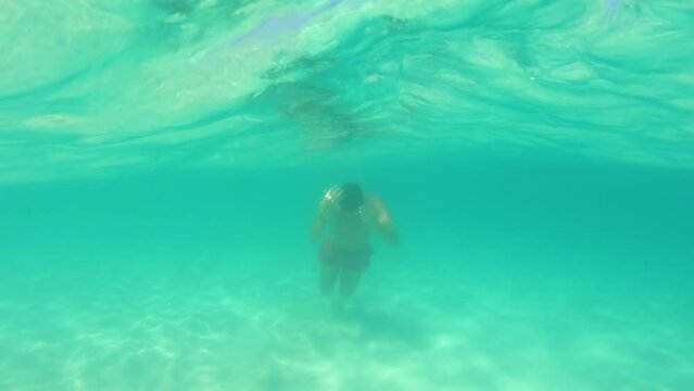 Half underwater, blurry turquoise ocean waves, slow motion close up video. Well trained boy in red trunks swim to sea. Thailand, Bamboo Island - excellent travel destination for daily trip