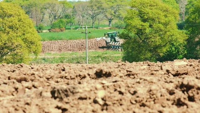 Low angle. A farmer tills his field with a tractor and Harrow disc, Cornwall, England, UK.