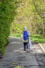 A woman with a backpack walks along the alley of the park on a spring morning