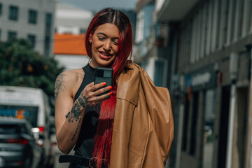 Fototapeta premium happy red-haired woman using mobile phone on the street