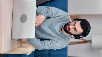VERTICAL VIDEO POV smiling modern man in headphones talking online video call use laptop on couch 