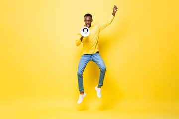 Powerful energetic young African man jumping and yelling on megaphone in studio yellow color...