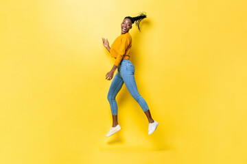 Fototapeta na wymiar Energetic happy African American woman jumping and smiling in yellow isolated studio background