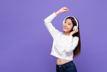 Cheerful happy smiling Asian woman listening to music on headphones and dancing in purple color studio isolated background