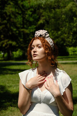 Naklejka premium Elegant young red hair lady in a white summer dress in a park