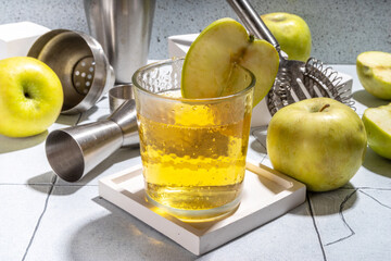 Apple cider cocktail. Raw apple vinegar cocktail garnished with apple slice, with bar utensils, copy space
