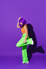 Carefree woman dancer wearing colorful sportswear having fun against purple background