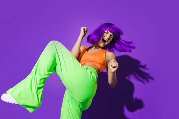 Carefree woman dancer wearing colorful sportswear having fun against purple background