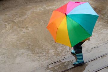A 3-year-old girl hides in the rain under a colored umbrella