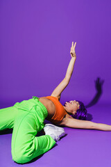 Carefree woman dancer wearing colorful sportswear performing against purple background